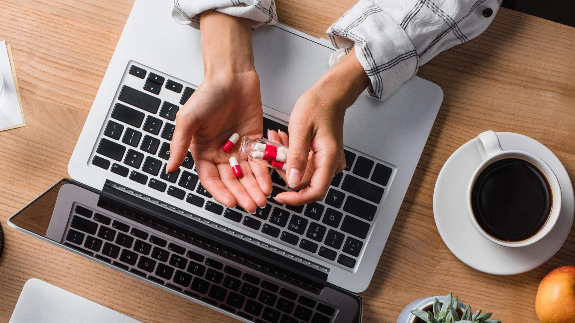 Person vid en laptop med piller i handen