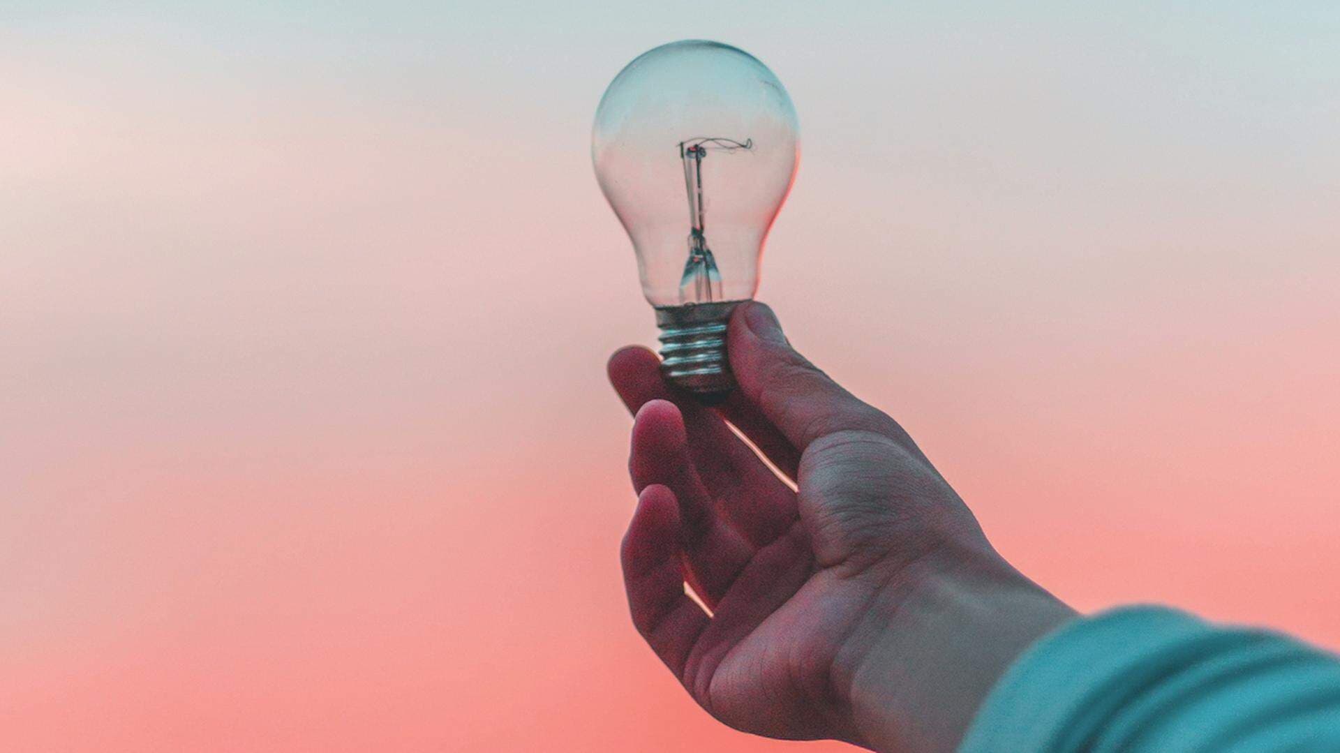 En hand som håller ut en glödlampa in en solnedgång