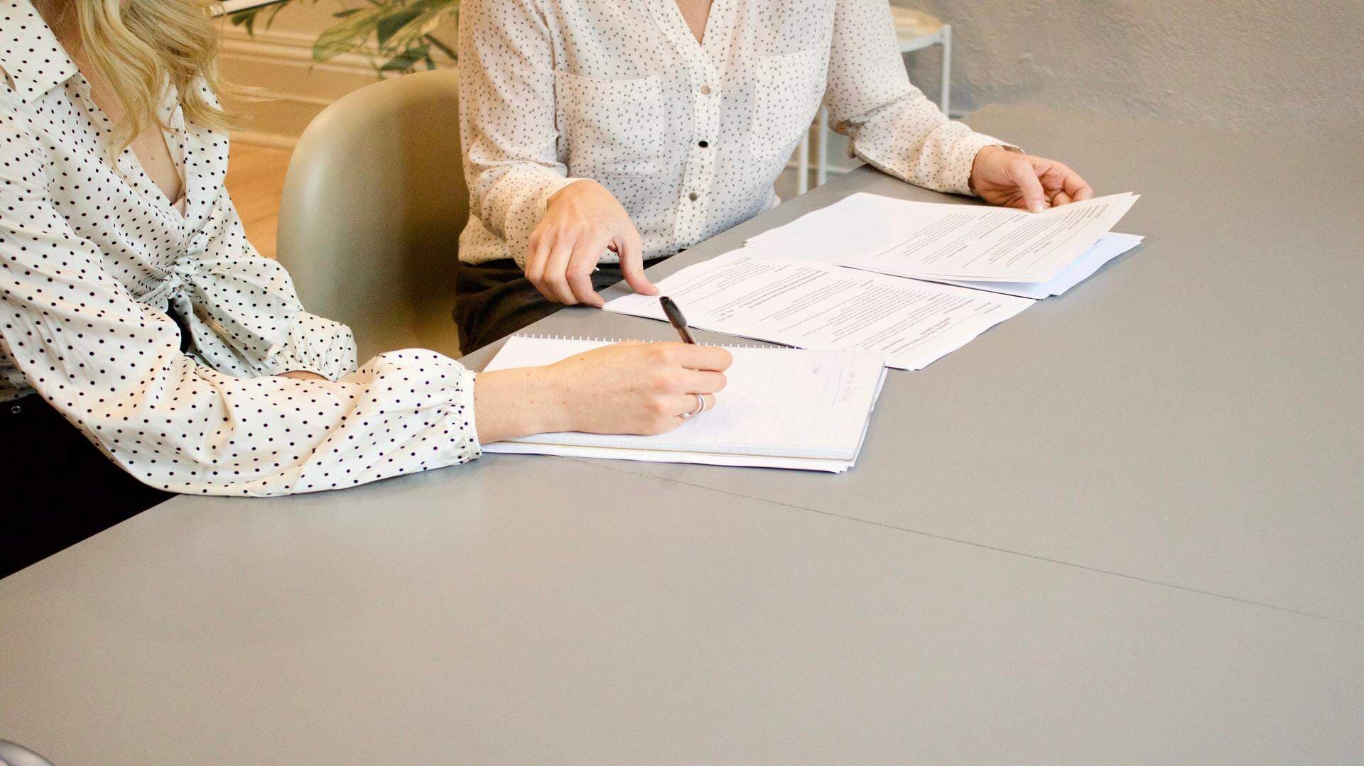 Två kvinnor sitter vid ett bord och går igenom en hög med papper