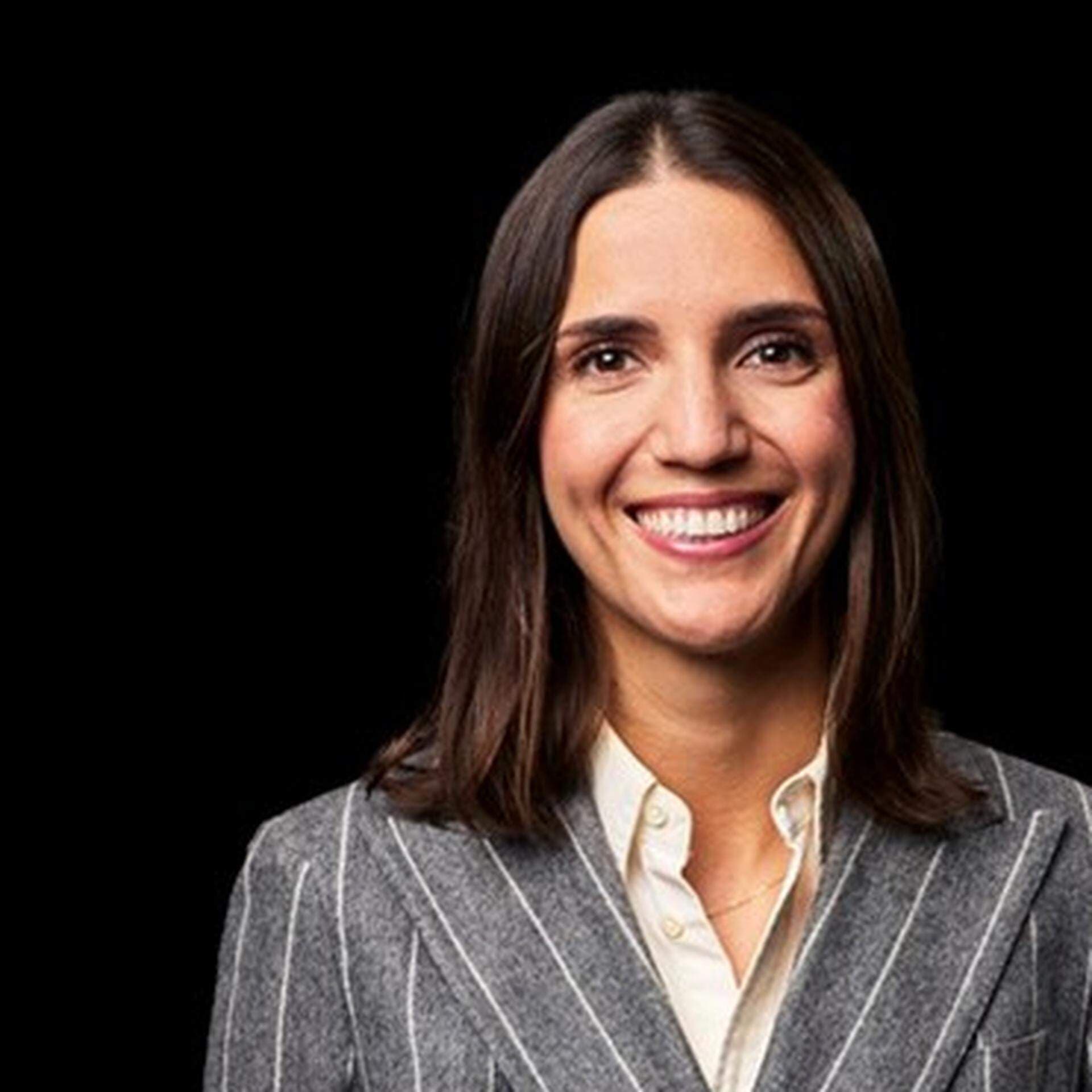 Diana Vasilou, med axellångt brunt hår, vit skjorta samt ljusgrå och vitrandig kavaj