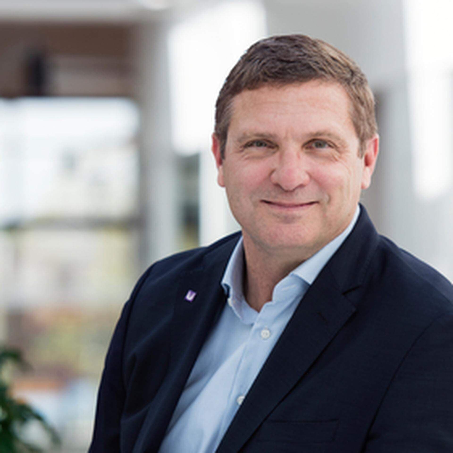 Eino i kontorsmiljö iklädd ljusblå skjorta och mörkblå kavaj