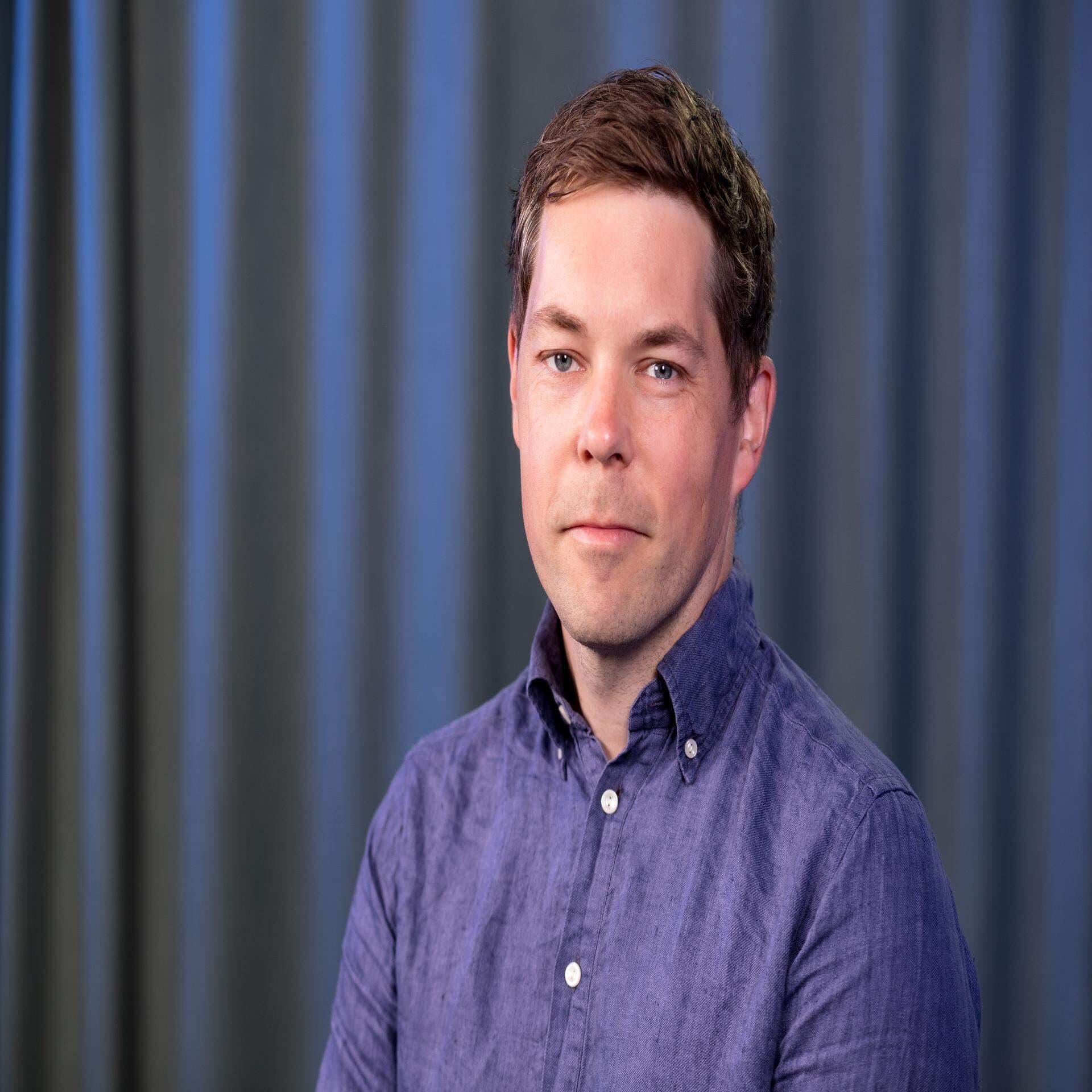 Anders Håkansson iklädd lila skjorta och med ett mörkblått draperi i bakgrunden