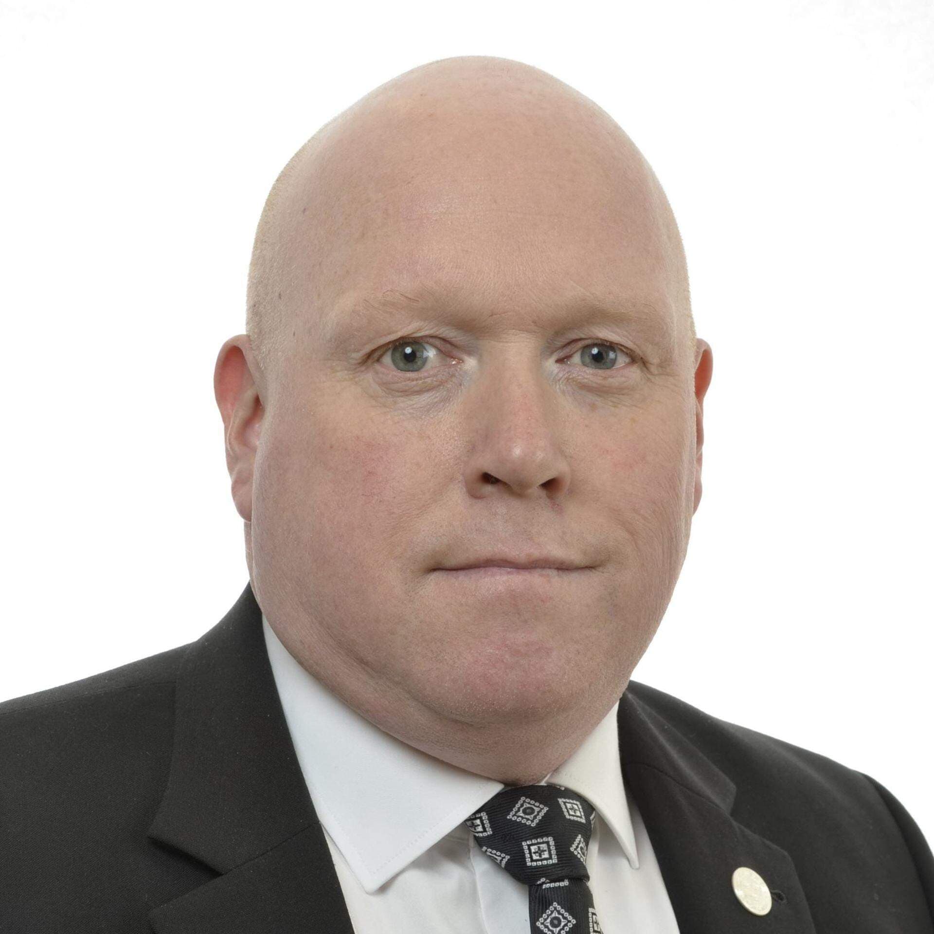 Magnus Persson i mörk kostym och vit skjorta. Bakgrunden är vit