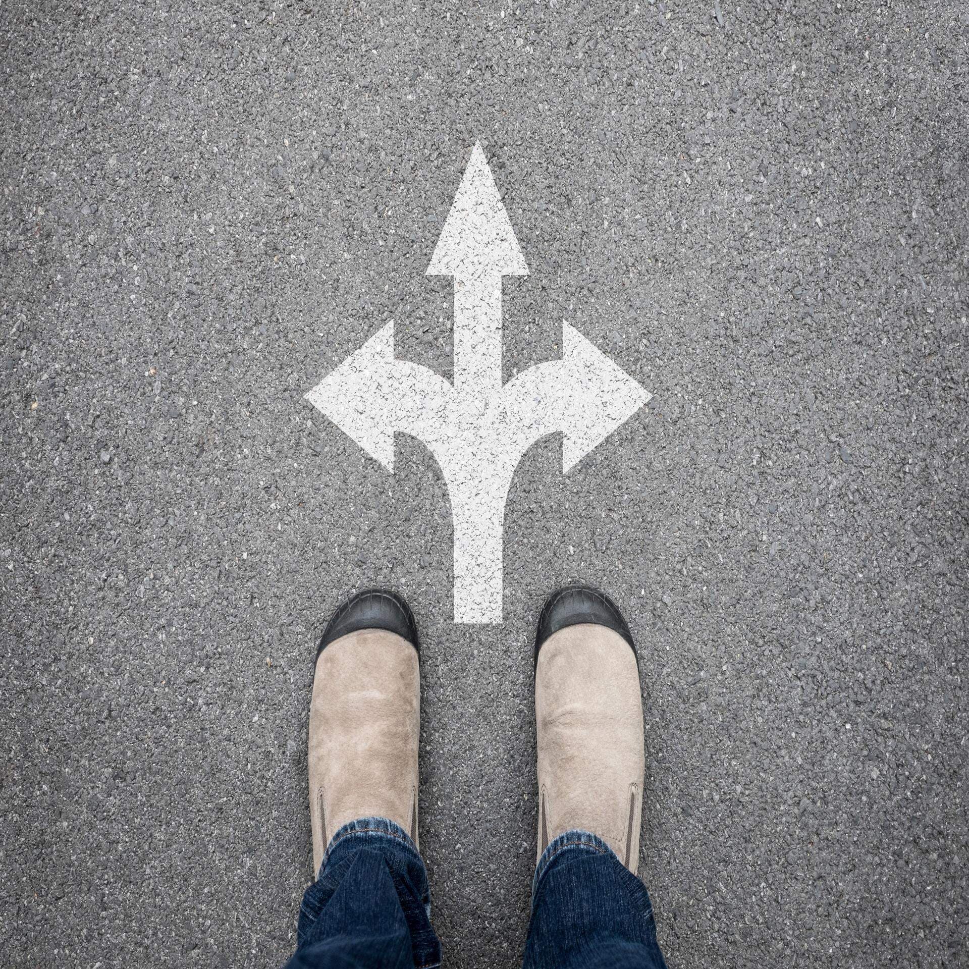 Bild på en persons fötter på en gata med direktionspilar till höger och vänster