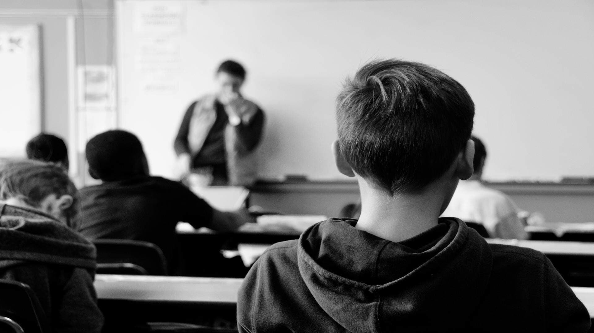 En skolklass fotad bakom en elev som sitter på skolbänk.