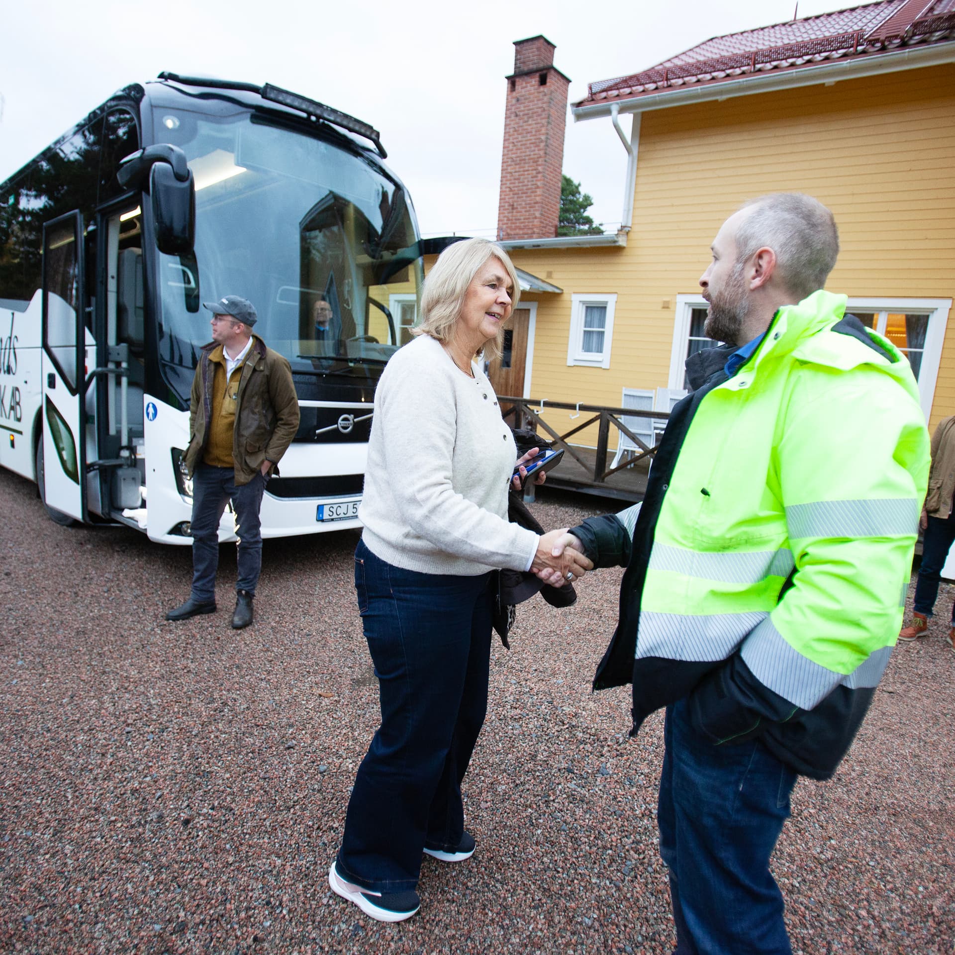 Landshövding Marita Ljung skakar hand med Gällö Timbers sågverks representant framför en buss.