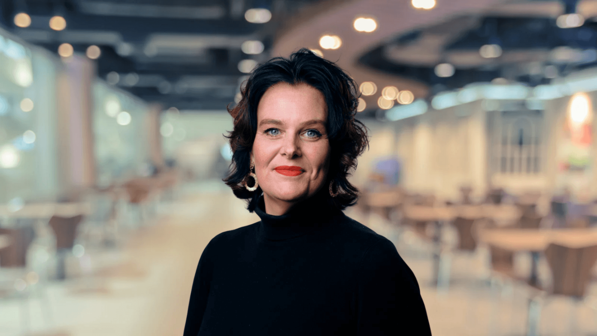 Ulrica Bennesved i förgrunden, ett suddigt rum med belysning i taket i bakgrunden.